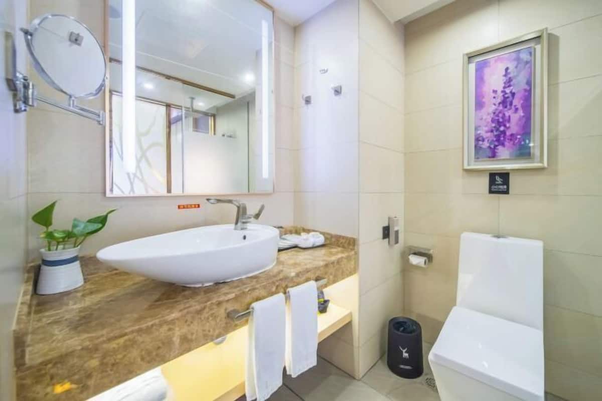 A modern bathroom with a large sink, a mirror, a toilet, and a framed artwork on the wall.