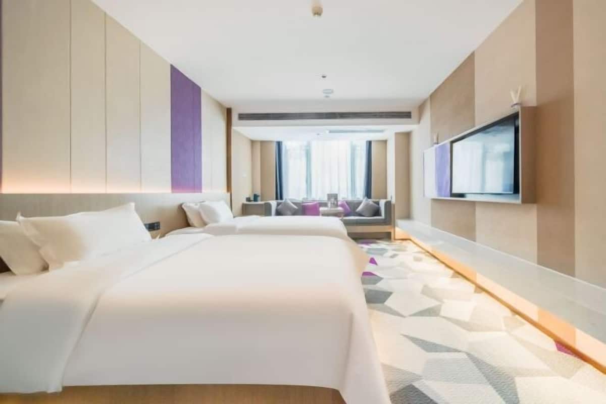 A hotel room with a large bed, a TV mounted on the wall, and a view of the city through the window.
