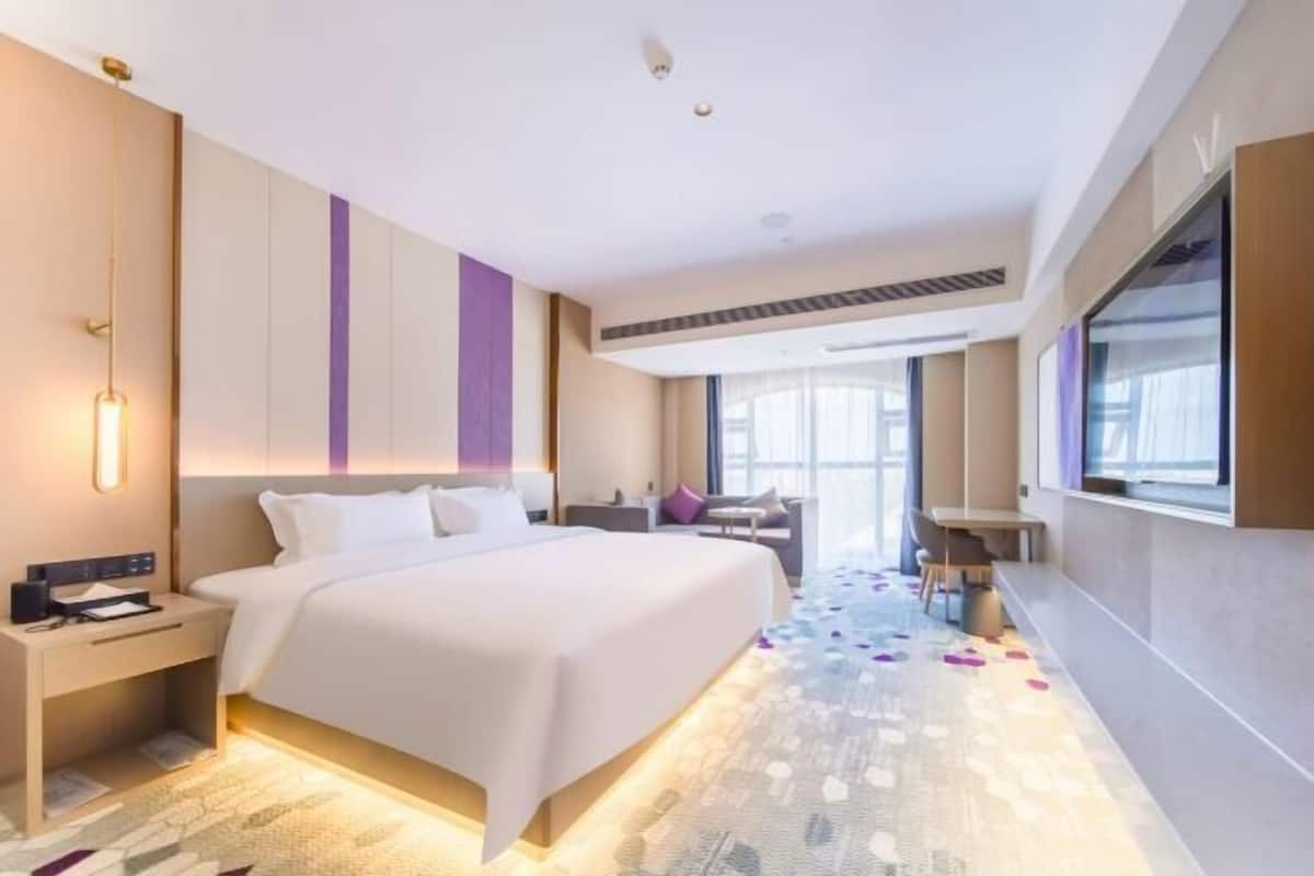 A modern hotel room with a large bed, a desk, and a large window.