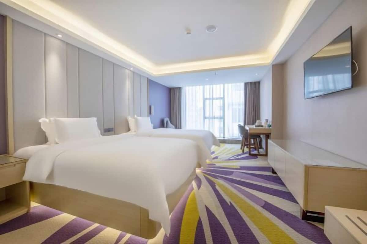 A hotel room with two beds, a desk, and a television.