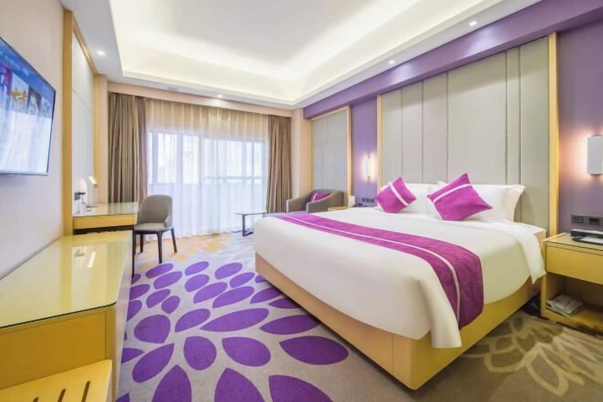 A hotel room with a large bed, a desk, a chair, and a window with curtains.