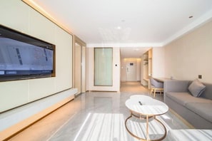 A modern hotel room with a large flat-screen TV mounted on the wall, a round coffee table, a sofa, and a minimalist design. - Lavande Hotel Dongguan Xiegang Branch (Dongguan)