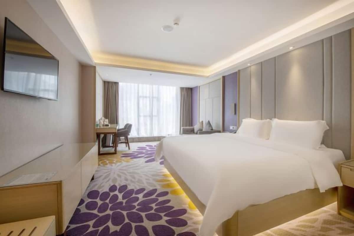 A hotel room with a large bed, a desk, and a television mounted on the wall.