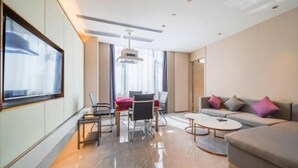 A modern hotel room with a sofa, a dining table, chairs, a TV, and a ceiling light. - Lavande Hotels (Dongguan)