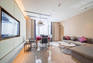 A modern hotel room with a sofa, a dining table, chairs, a TV, and a ceiling light. - Lavande Hotels (Dongguan)