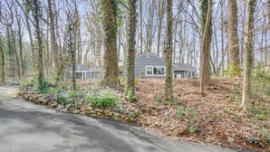 A residential area with two houses surrounded by tall trees and a stone wall. - Family-Friendly Knoxville Home: Close to UT! (Knoxville)