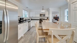 A modern kitchen with white cabinetry, stainless steel appliances, and a wooden dining table. - Family-Friendly Knoxville Home: Close to UT! (Knoxville)