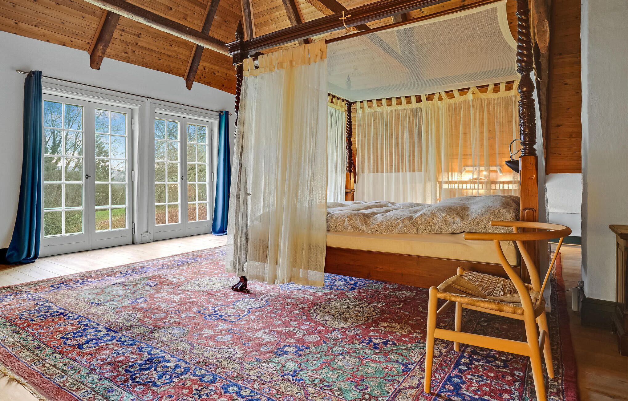 Une chambre spacieuse avec un lit à baldaquin, une grande fenêtre avec des rideaux et un plafond en bois de style traditionnel.