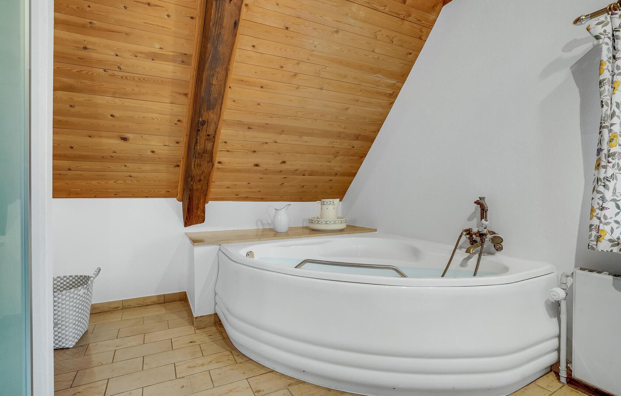A bathroom with a wooden ceiling, a white bathtub, a sink, and a radiator.