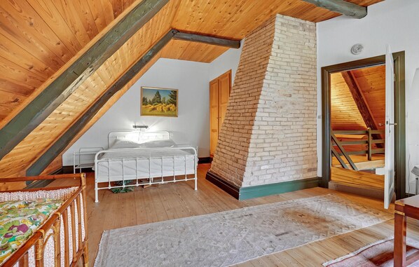A bedroom with a sloped ceiling, a bed, a brick wall, and a door leading to another room.