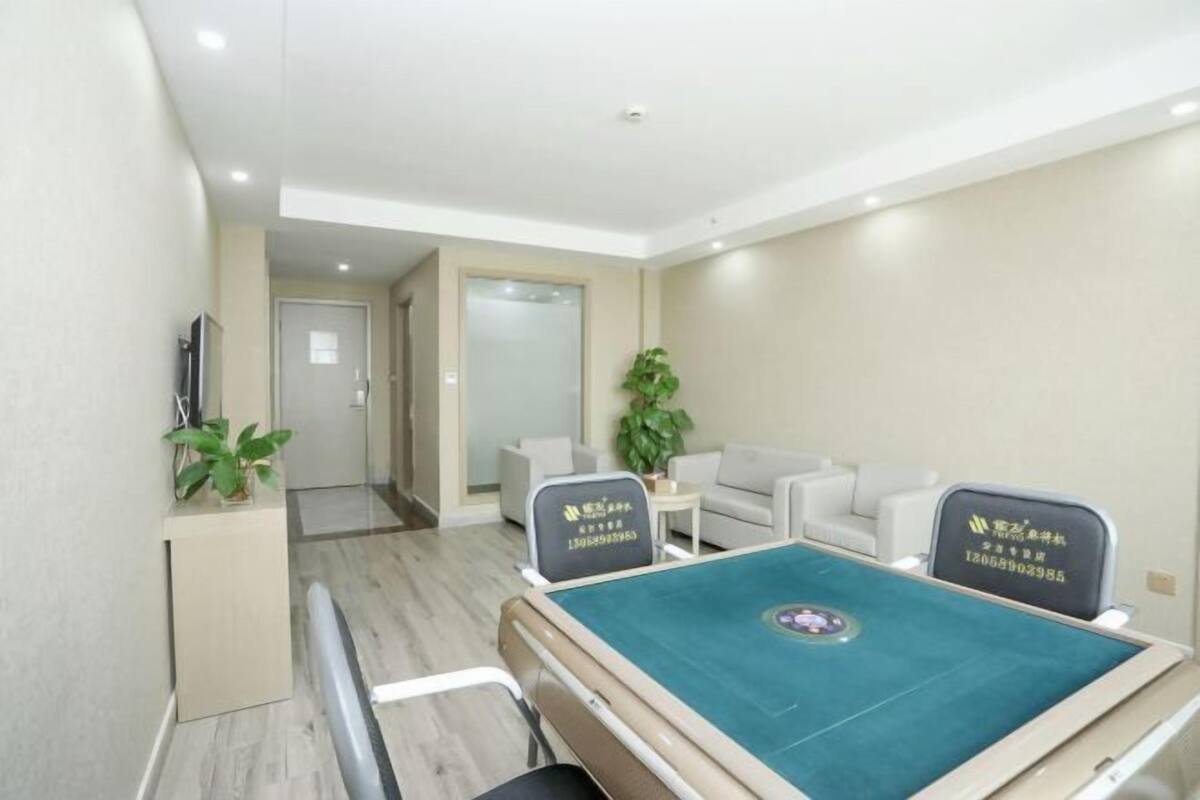 Una habitación de hotel con mesa de billar verde, un sofá, dos sillones, una mesita y una planta en maceta.