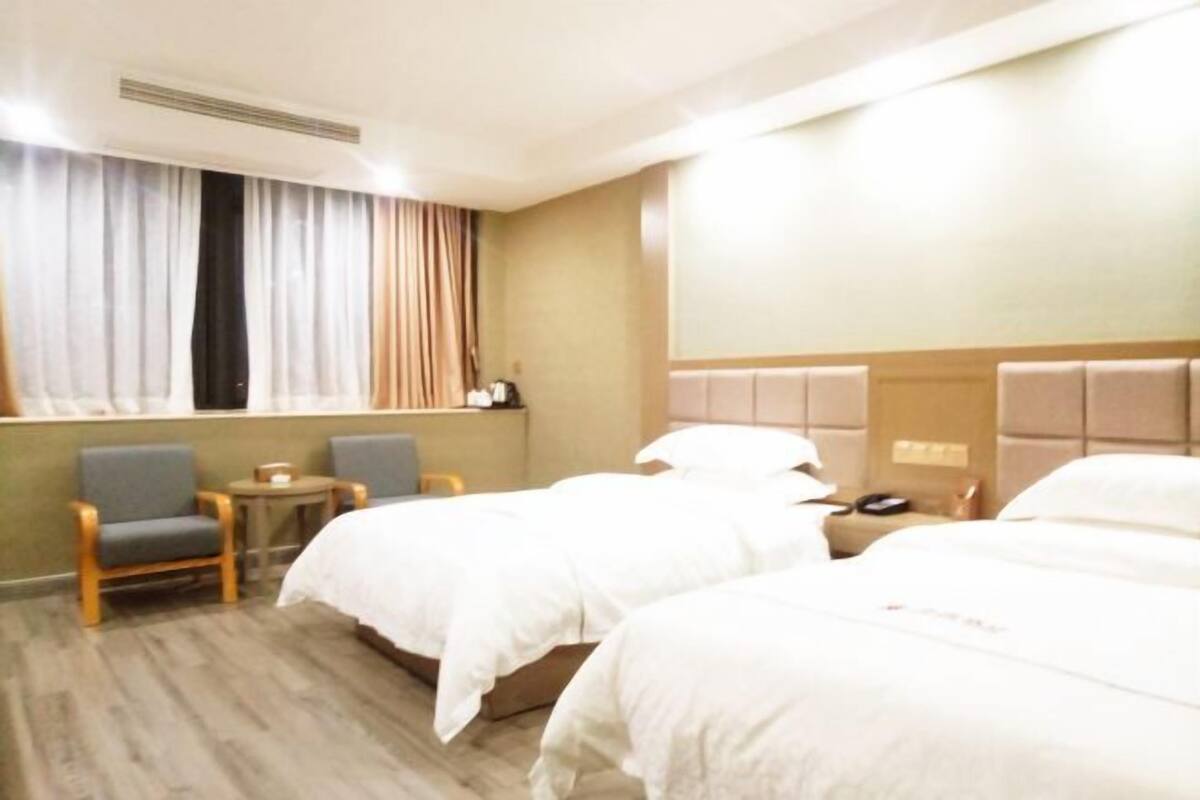 Una habitación de hotel con dos camas, una mesita, una silla y una ventana con cortinas.