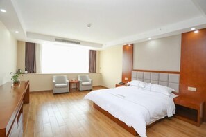 A hotel room with a large bed, two chairs, a small table, a desk, and a window with curtains.