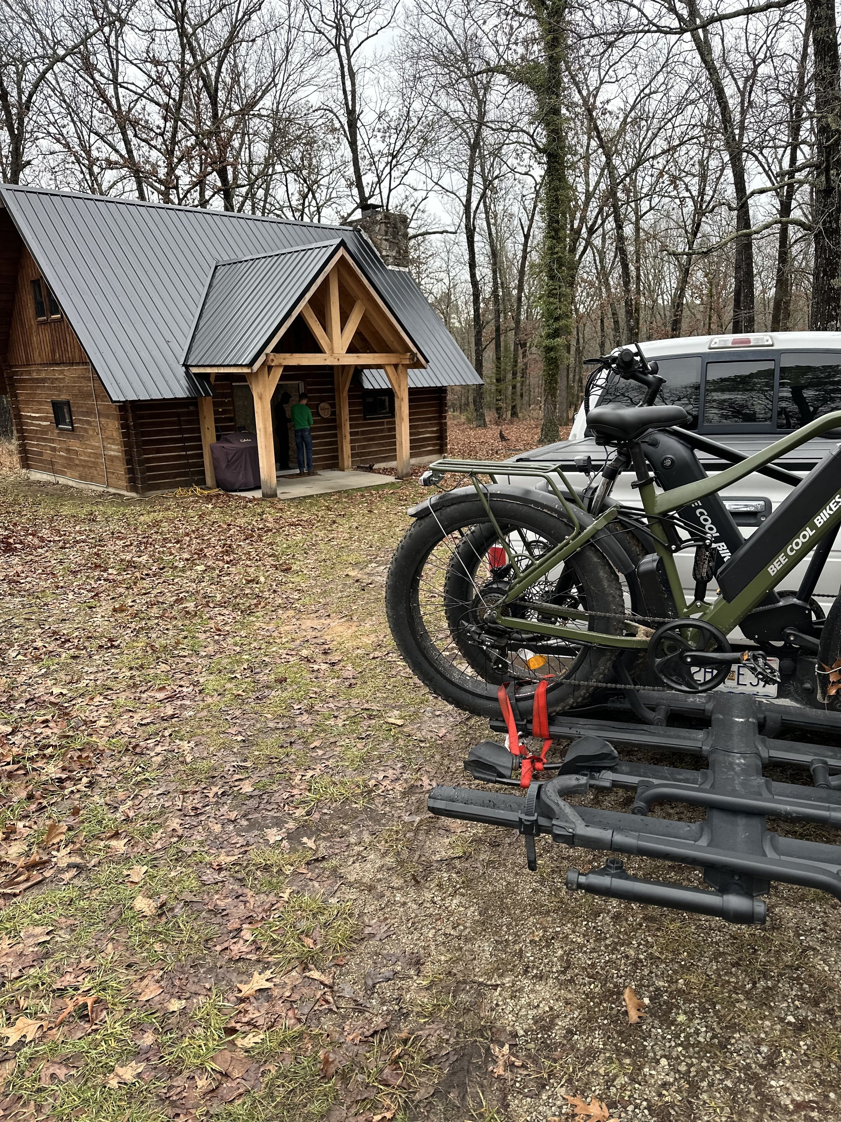 Una cabaña rústica con techo de metal, una bicicleta sujeta a un soporte y un vehículo estacionado cerca.