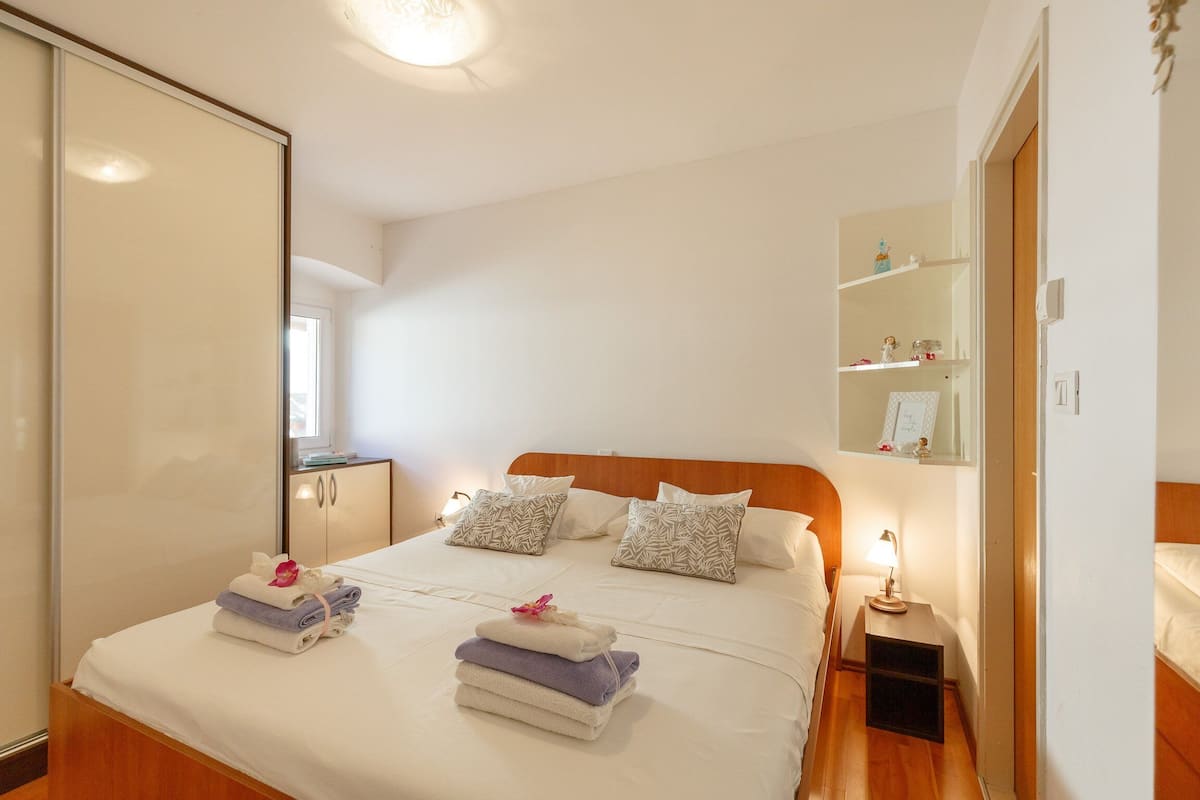 A neatly made bed with folded towels and pillows, a bedside table with a lamp, and a wardrobe with a mirror.