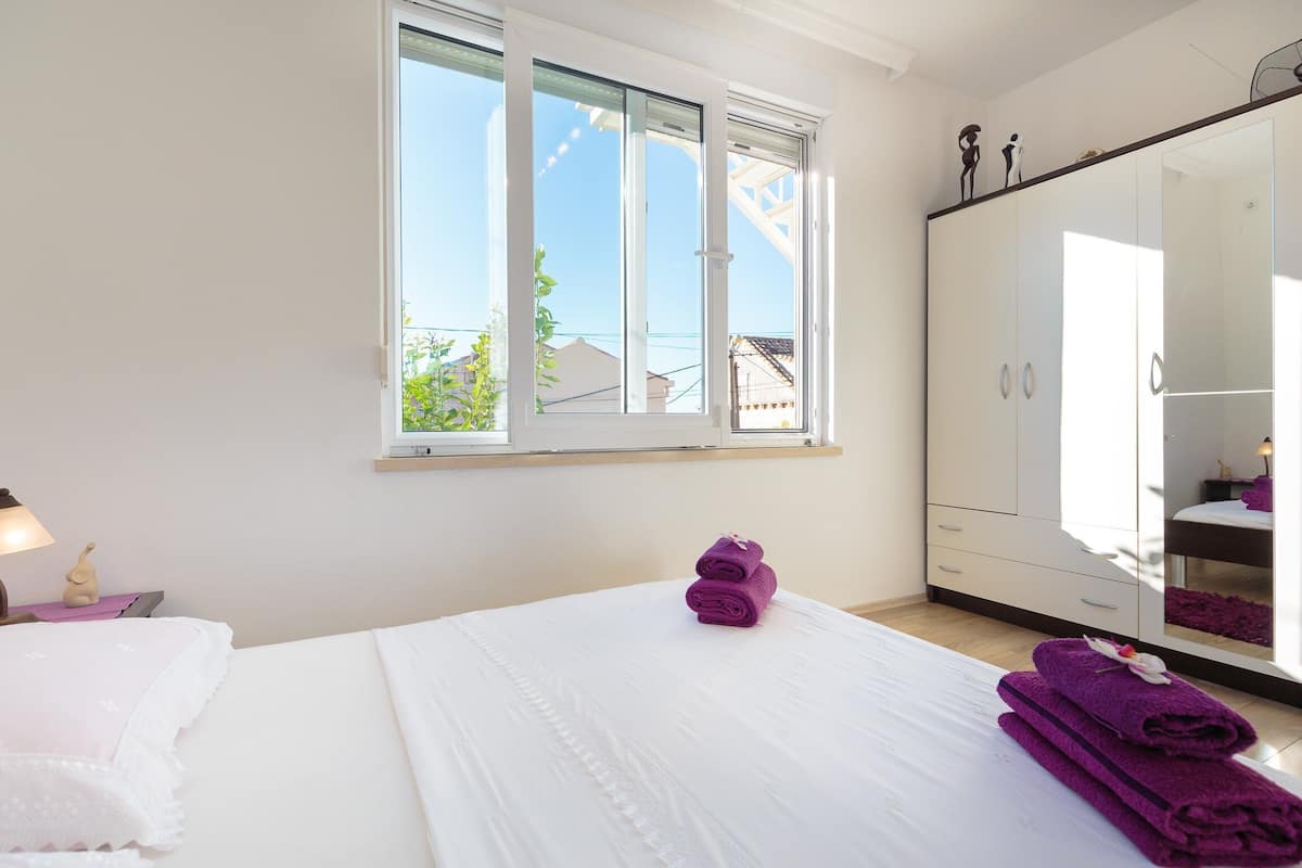 A bedroom with a large bed, a wardrobe, and a window with a view of buildings.