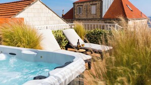Un bain à remous avec des chaises longues et une table où sont disposées des boissons, le tout entouré d’une haute herbe et d’un bâtiment doté d’un toit rouge.