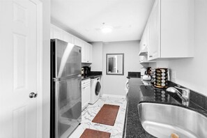 Compact kitchen with a refrigerator, washing machine, and sink, complete with a modern faucet and ample storage.