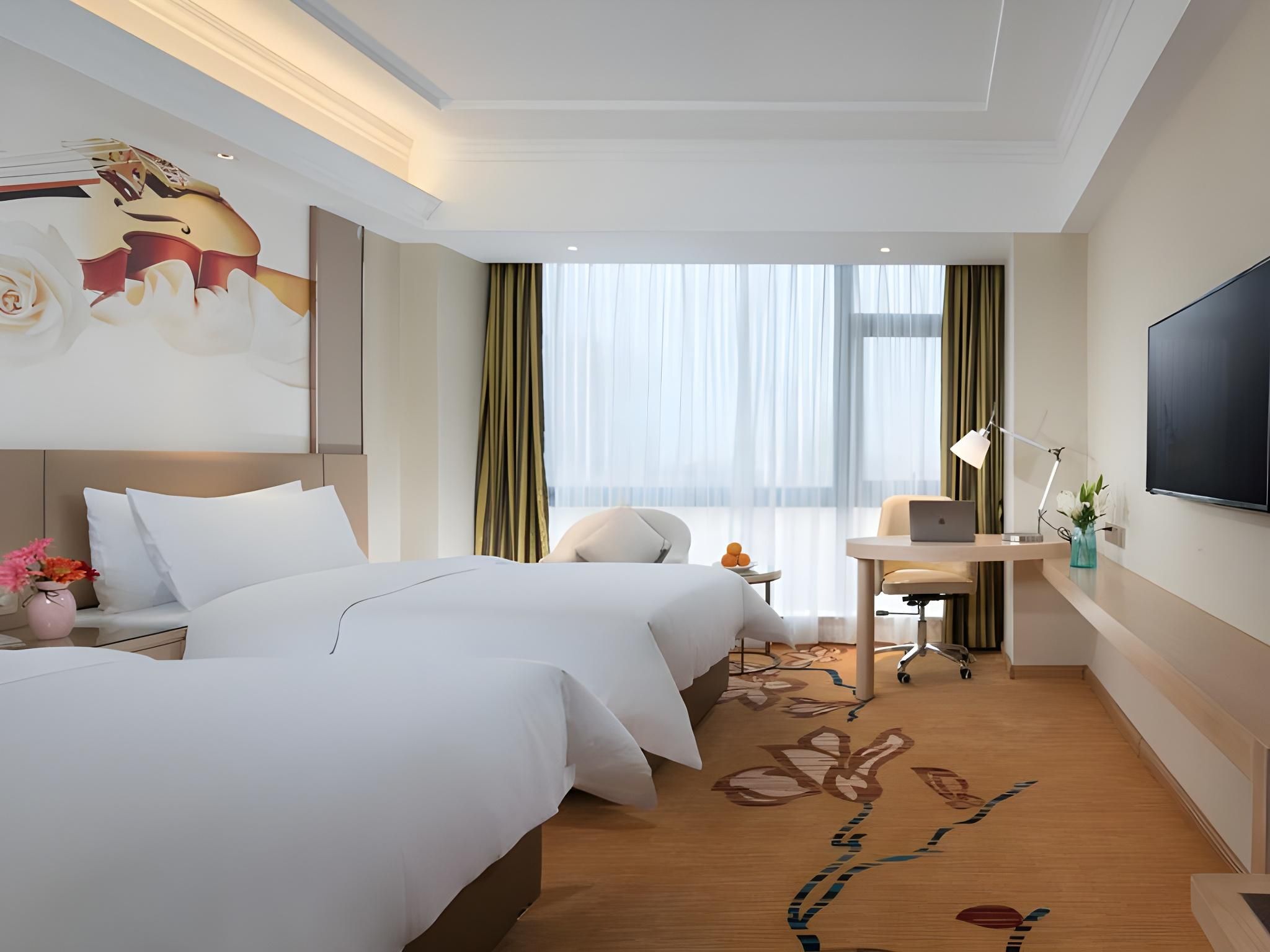 A hotel room with two beds, a desk with a laptop, a TV, and a large window with curtains.