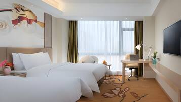 A hotel room with two beds, a desk with a laptop, a TV, and a large window with curtains.