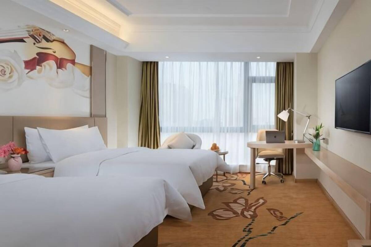 A hotel room with two beds, a desk, a TV, and a large window with curtains.