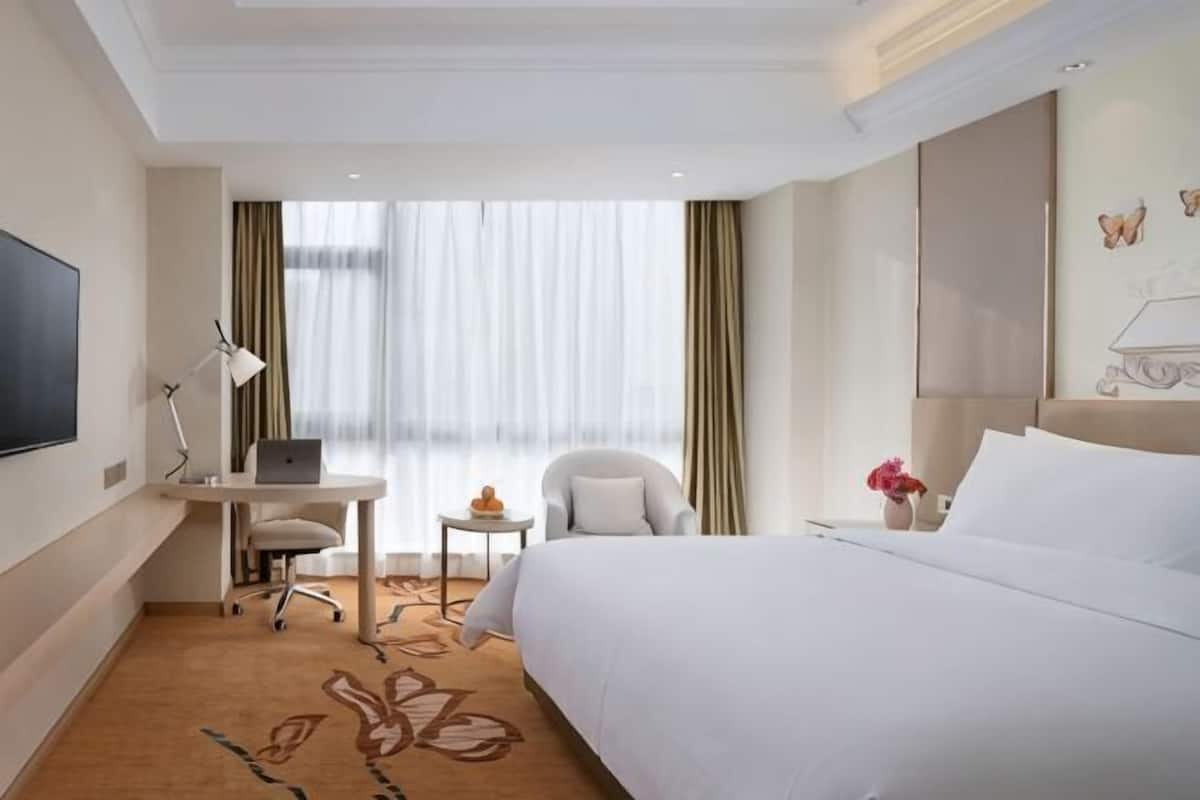 A hotel room with a bed, desk, chair, TV, and a small table with flowers.