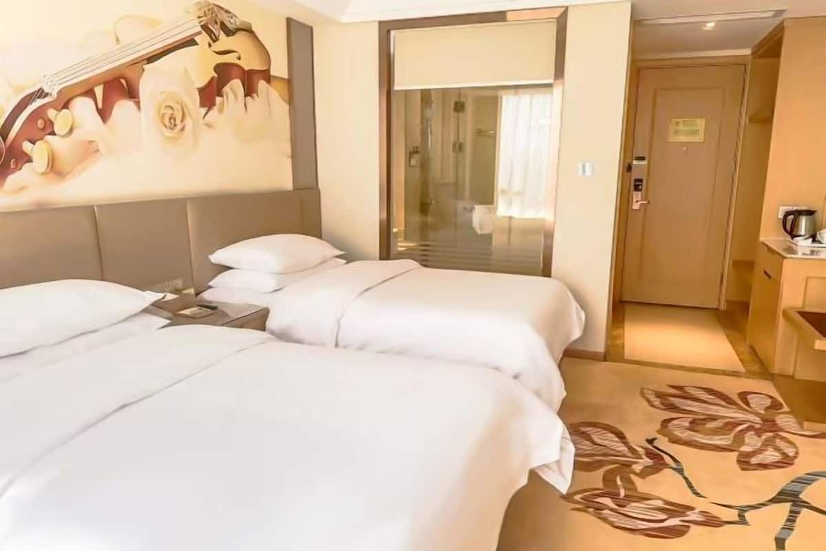 A hotel room with two beds, a guitar artwork on the wall, a sliding door to the bathroom, and a floral carpet.