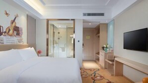 A hotel room with a large bed, a television, a desk with a chair, and a bathroom visible through an open door.