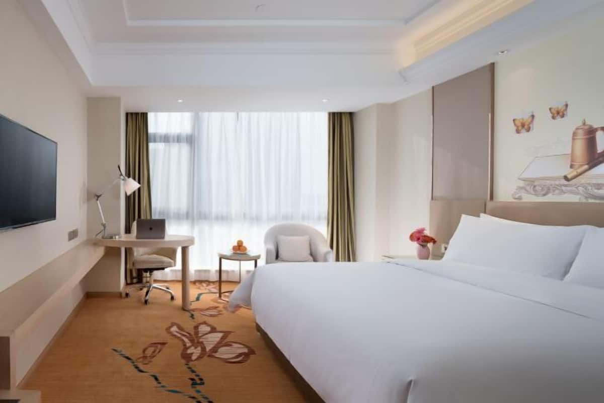 A hotel room with a bed, desk, chair, TV, and a window with curtains.