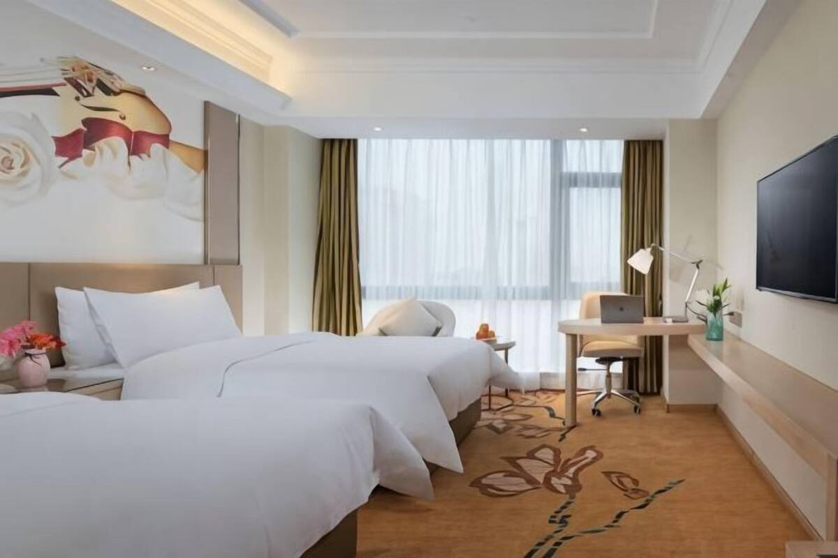 A hotel room with two beds, a desk, a chair, a TV, and a large window.
