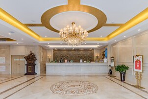 Un hall de hotel con una recepción, una araña de cristal, un revestimiento decorativo y un suelo estampado.
