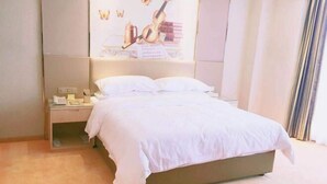 A neatly made bed in a hotel room with a headboard, a bedside table with a lamp, and a poster on the wall.