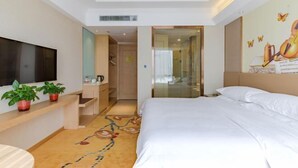 A hotel room with a bed, a TV, a desk with a chair, and a small plant.