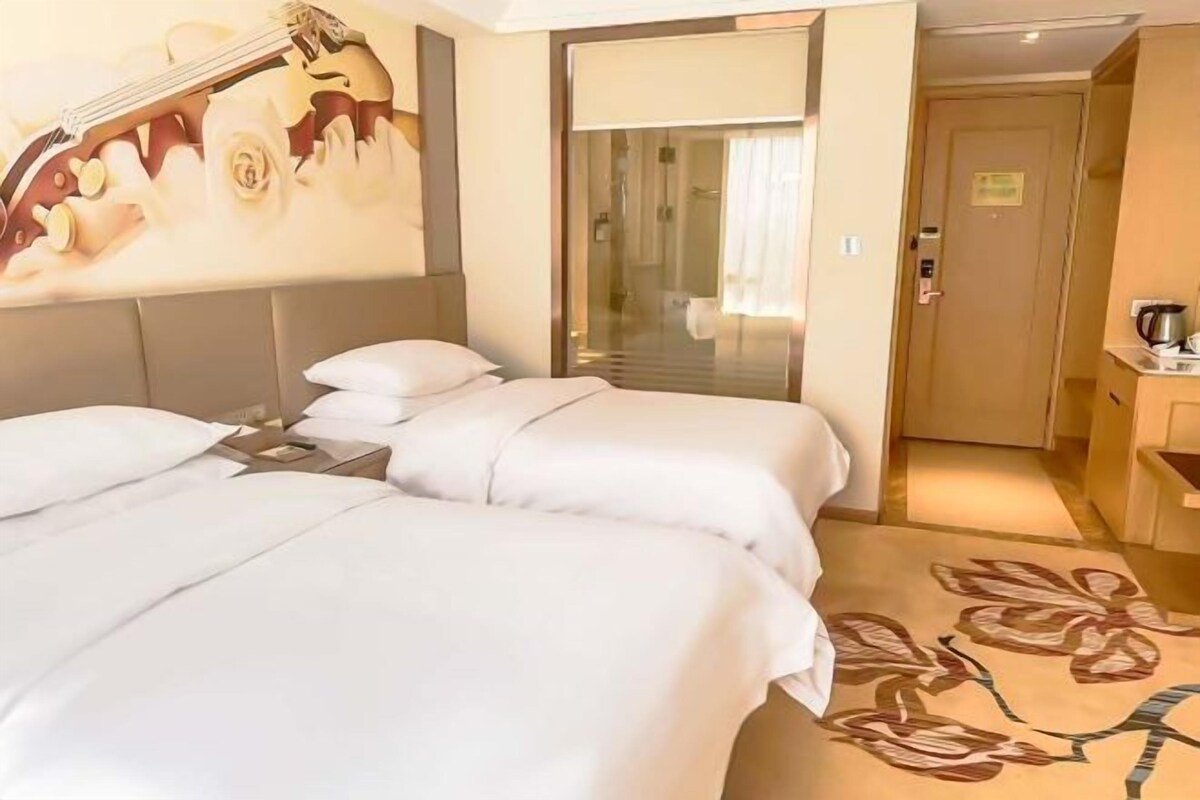 A hotel room with two beds, a guitar artwork on the wall, a sliding door to the bathroom, and a floral carpet.