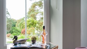 A room with a large window, a table with a book, a wine bottle, and a duck figurine. - Wansfell at Lipwood House (Windermere)