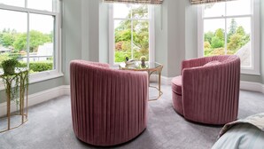 A room with two round, plush armchairs, a small table, and a view of greenery outside. - Wansfell at Lipwood House (Windermere)
