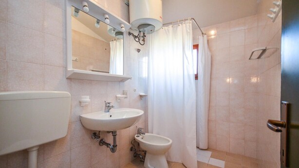 A bathroom with a toilet, sink, bidet, and shower curtain.