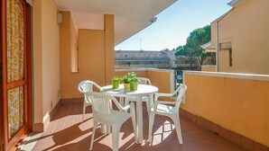 Un balcon avec une table et des chaises blanches, des plantes en pot et une vue sur les bâtiments en arrière-plan.