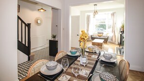 A dining area with a checkered floor, a dining table set with plates, glasses, and a vase of flowers. There is a staircase with a black railing leading to another room. - Wolf Cottage (Weymouth)