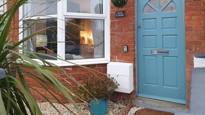 A cottage with a blue door, a window with curtains, and a small potted plant in front. - Wolf Cottage (Weymouth)