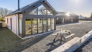 Ein modernes Haus mit einem großen Panoramafenster, einer Schotterauffahrt und einem Picknicktisch.