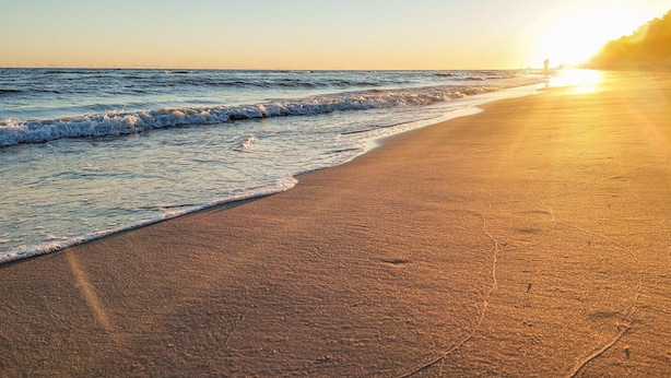 Ein Strand mit Wellen und einem Sonnenuntergang.