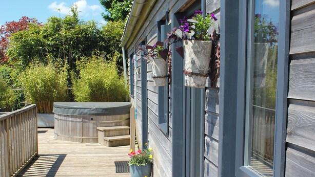En træterrasse med et boblebad, plantekrukker og et træhegn.