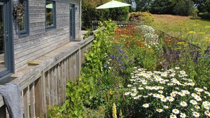 Et træhus med terrasse, omgivet af et væld af farverige blomster og planter.