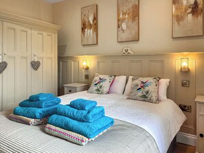 Un dormitorio con cama, almohadas, una mesita de noche, una lámpara y una lámpara de pared.