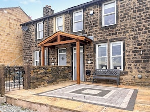 A stone house with a wooden porch, a stone wall, and a bench outside.