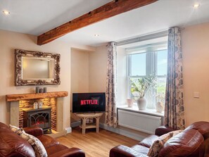A living room with a fireplace, a television, leather sofas, and a large window with curtains. - 19 Sykes Head Cottage - UK42149 (Oakworth)