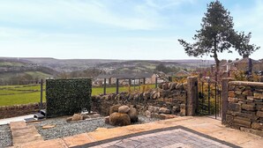 A stone wall, a hedge, and a view of a town in the distance.
