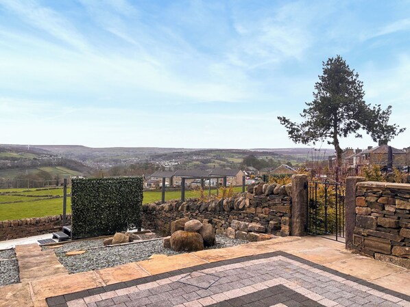A stone wall, a hedge, and a view of a town in the distance.