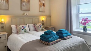 A bedroom with a bed, bedside lamps, a nightstand, a window with a view, and artwork on the wall.